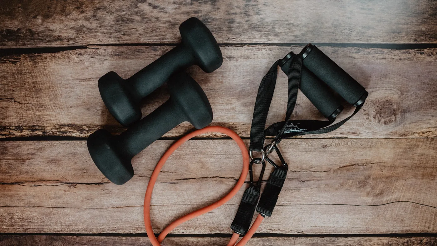 Resistance tubing, a loop band, and small hand weights laid out on a wooden surface.